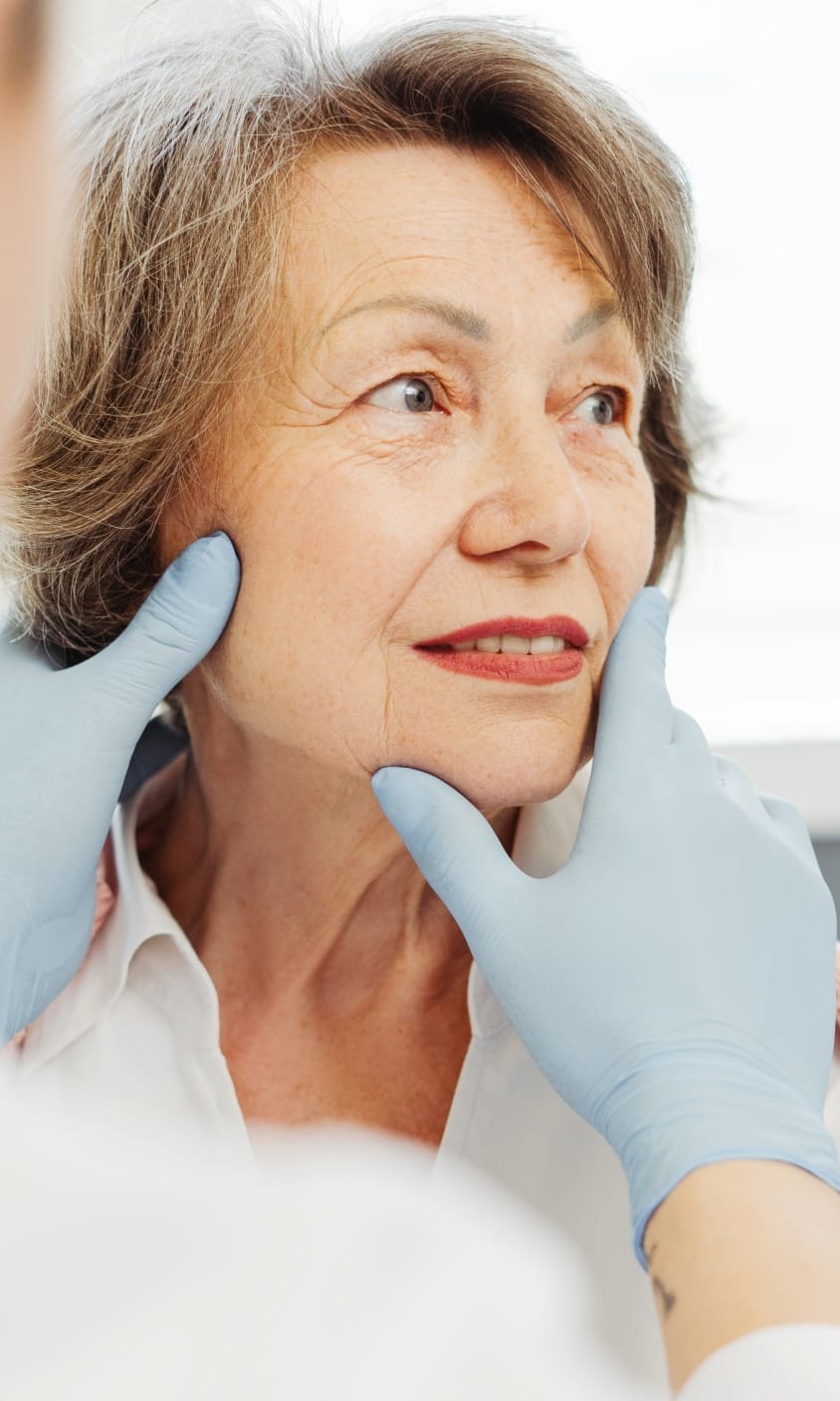 Older woman having the skin of her face examined by a gloved provider